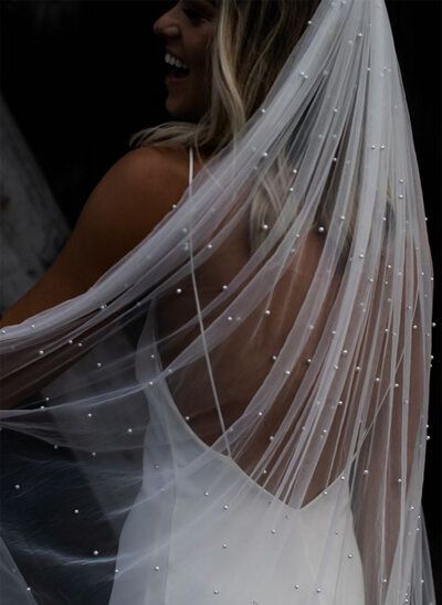 a woman wearing a wedding veil with pearls on the bottom and back of her dress