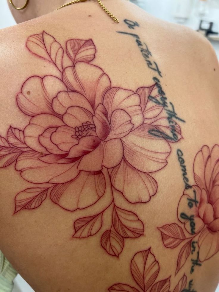 the back of a woman's shoulder with flowers and words tattooed on her arm