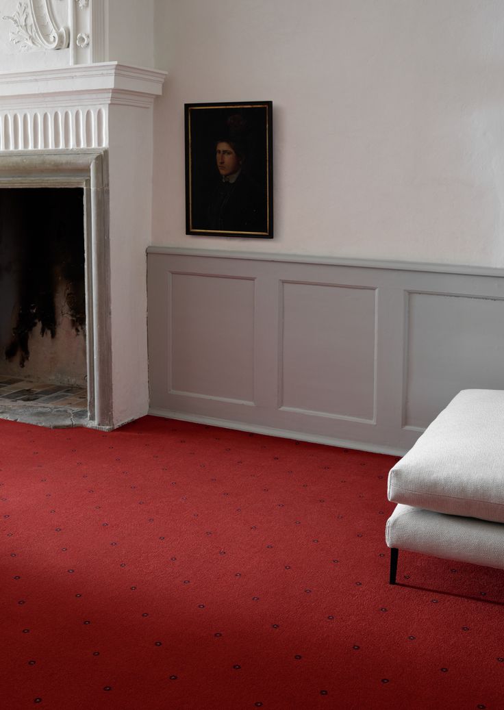 a living room with red carpet and white walls, an ornate fireplace and painting on the wall