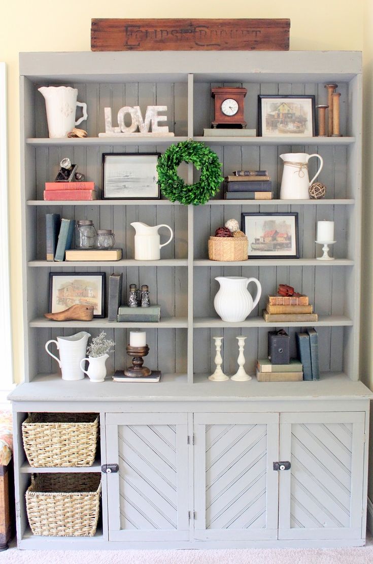 a gray bookcase filled with lots of books next to a white vase and other items