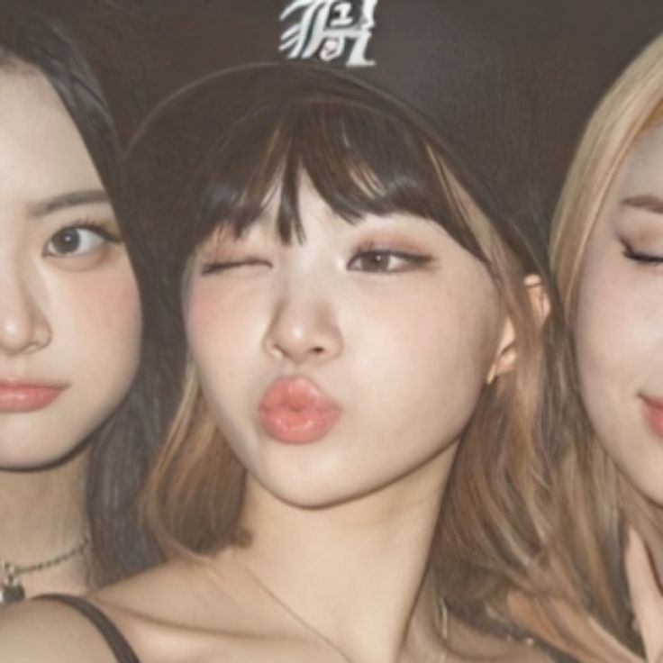 three young women with their mouths open and one wearing a hat, are posing for the camera