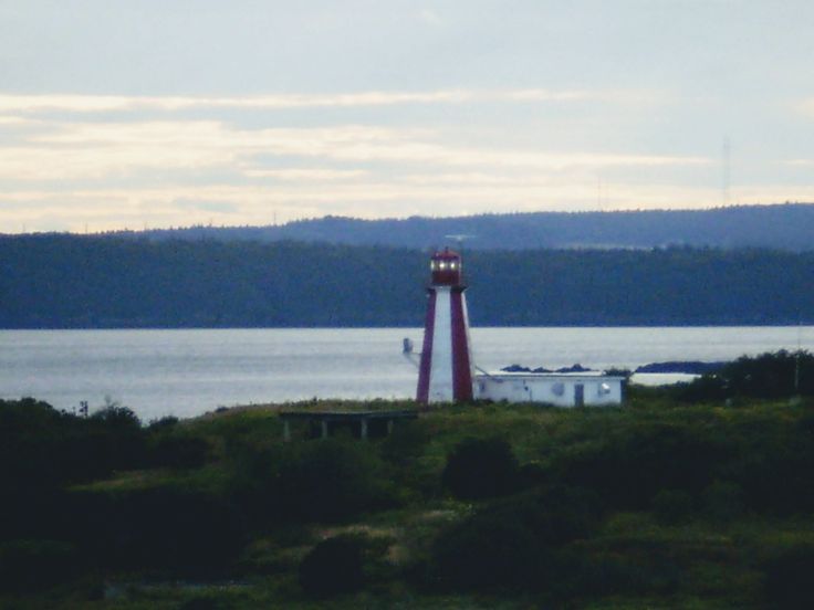 a red and white light house sitting on top of a lush green hillside next to the ocean