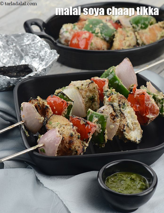 two black trays filled with meat and vegetables on skewers next to dipping sauce