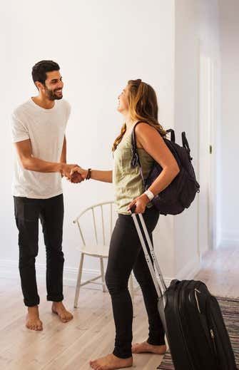 a man standing next to a woman holding a suitcase and shaking hands with each other