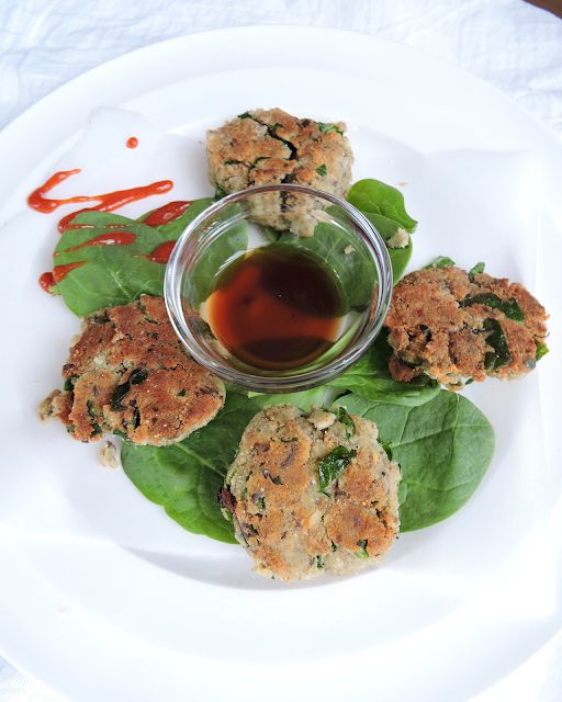 a white plate topped with crab cakes and spinach leaves next to a dipping sauce