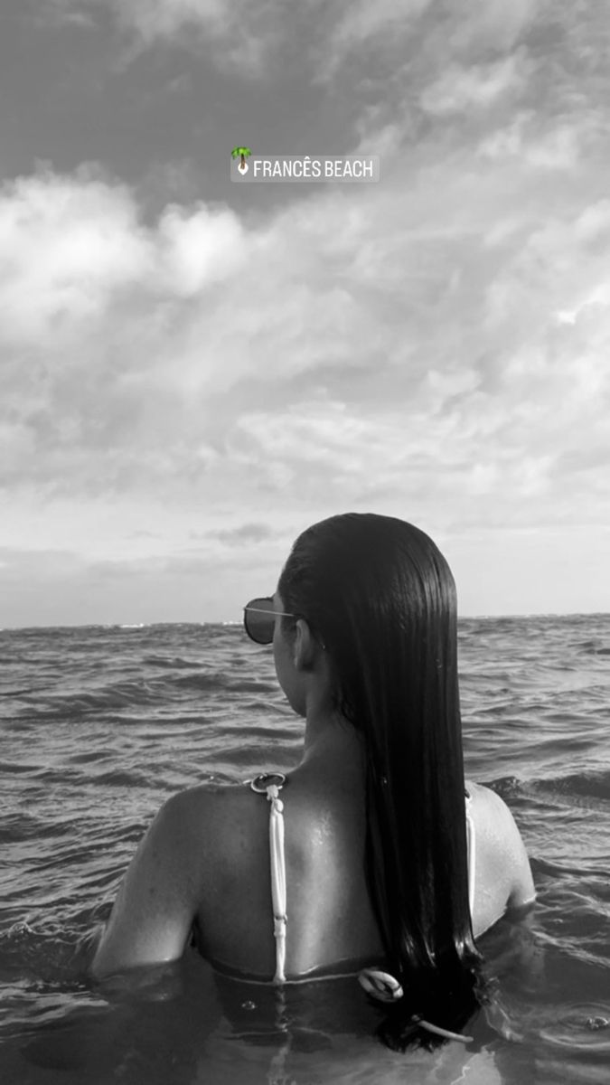 a woman sitting in the water with her back to the camera and looking at the sky