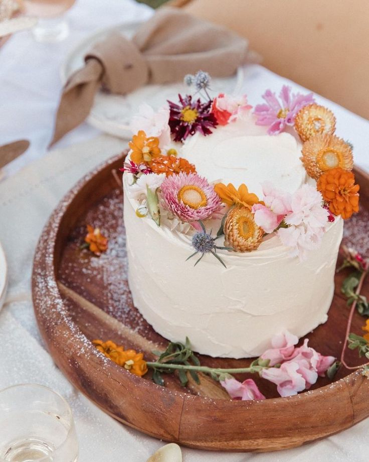 there is a white cake with flowers on the top and bottom, sitting on a wooden platter