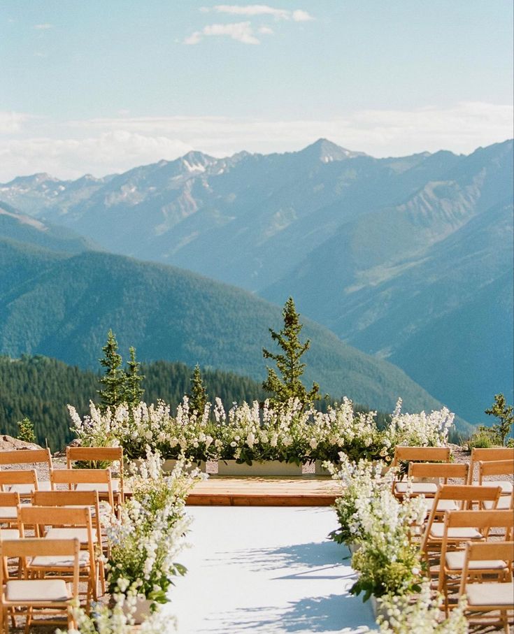 an outdoor ceremony set up with wooden chairs and flowers in front of the mountain range