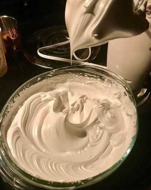 a glass bowl filled with whipped cream on top of a counter next to a mixer