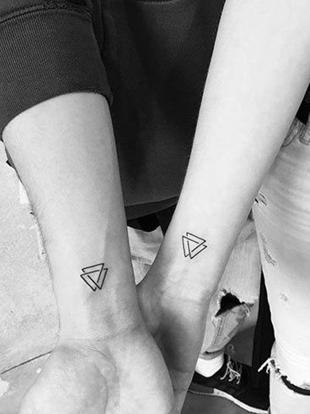 two people with matching tattoos on their arms holding each other's hands and looking down at the ground