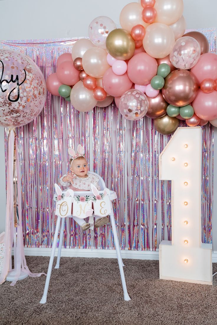 a baby in a highchair next to balloons and a number one sign for a 1st birthday party