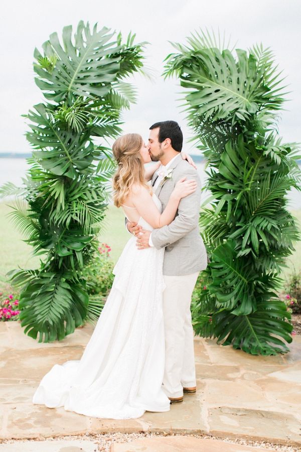 a bride and groom kissing in front of a tropical arch