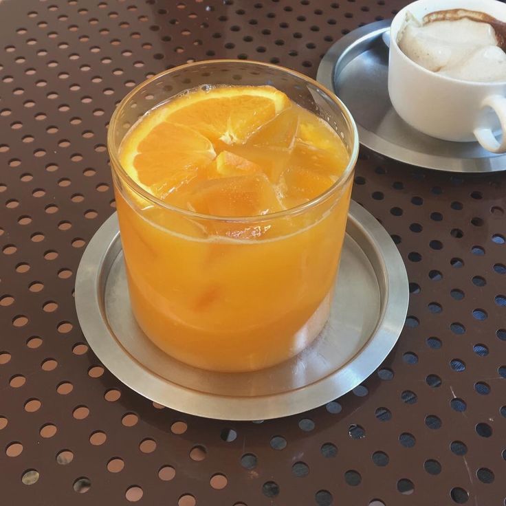 there is a glass of orange juice on the table next to a cup and saucer