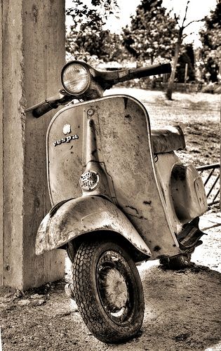 an old yellow scooter is parked next to a pole in the dirt near a tree