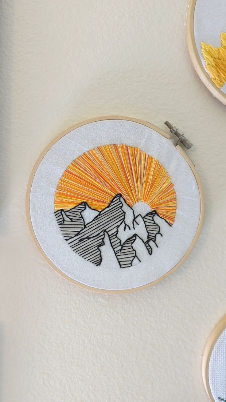 three hand embroidered wall hangings with mountains and sun in the middle, on top of each other