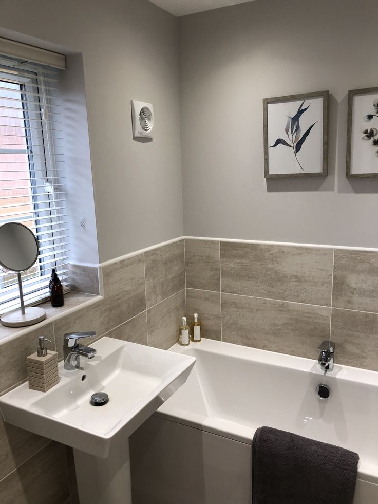 a white bath tub sitting under a window next to a sink and mirror in a bathroom