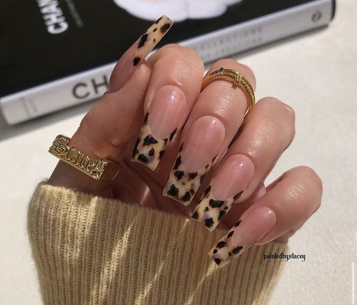 a woman's hand with leopard print nails and gold rings on it, next to a stack of books