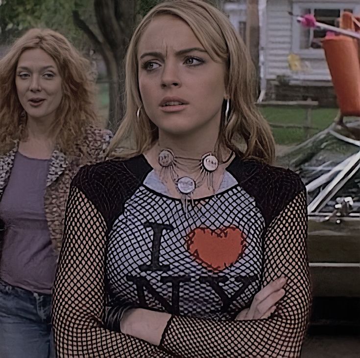 two women standing next to each other in front of a parked car and another woman with her arms crossed