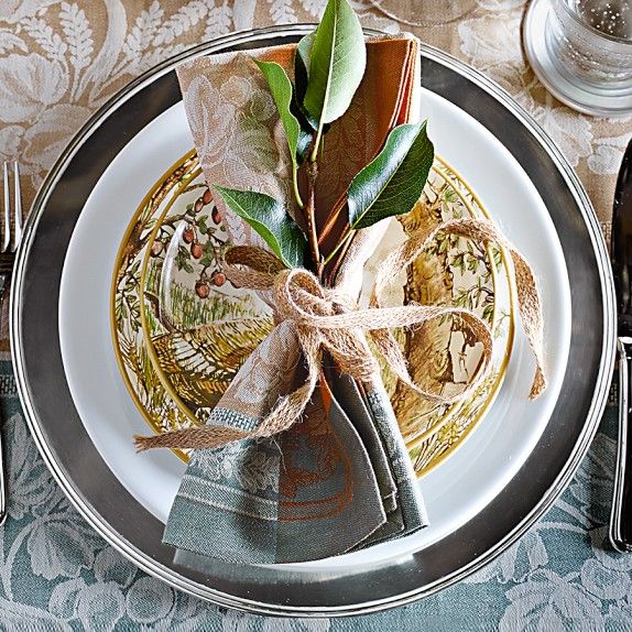 a place setting with napkins, silverware and green leafy decorations on a plate