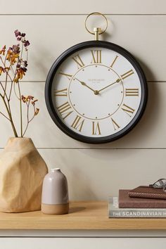 a black and white clock sitting on top of a wooden shelf next to a vase with flowers