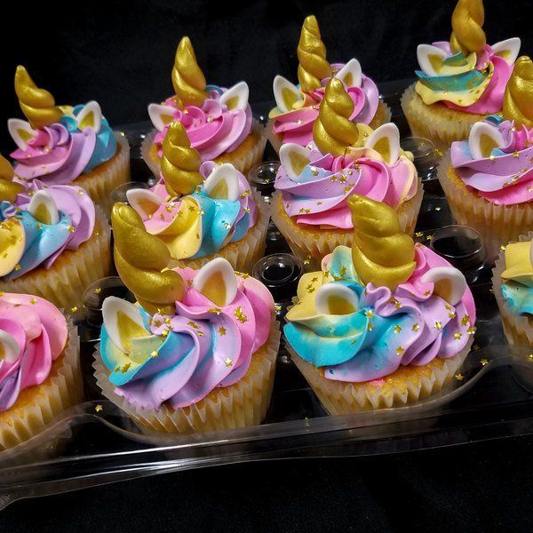 cupcakes decorated with pink, blue and yellow icing are in a plastic container