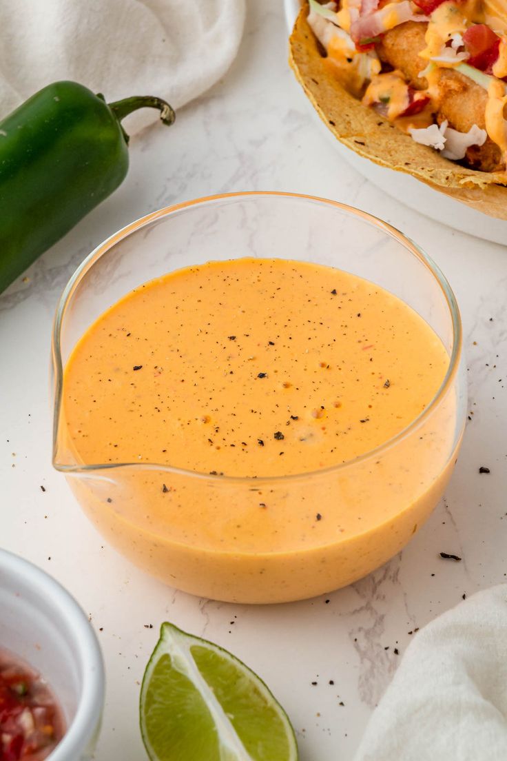 a glass bowl filled with sauce next to a tortilla shell and lime wedge