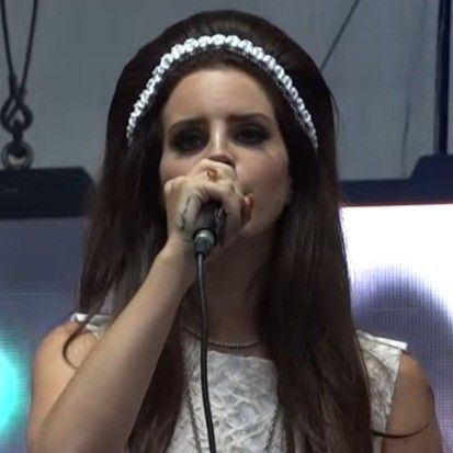 a woman with long brown hair holding a microphone in front of her face and wearing a headband