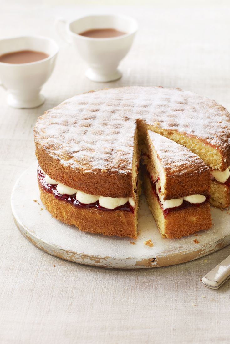 a cake that has been cut in half and is sitting on a plate with two cups of coffee behind it