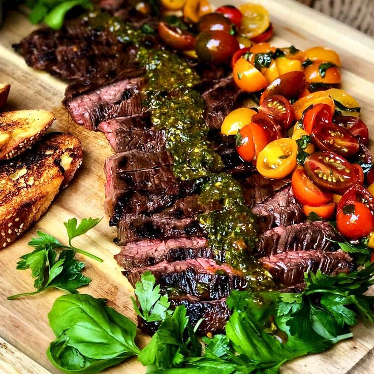 steak, tomatoes and basil on a cutting board next to some grilled meats