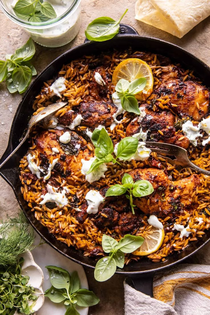 a skillet filled with chicken and rice topped with fresh herbs, lemon wedges and sour cream