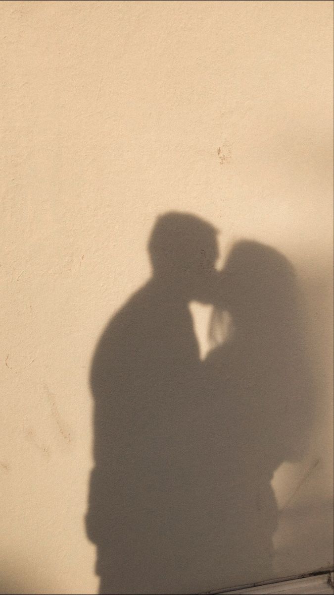 the shadow of a man and woman kissing in front of a white wall with shadows on it