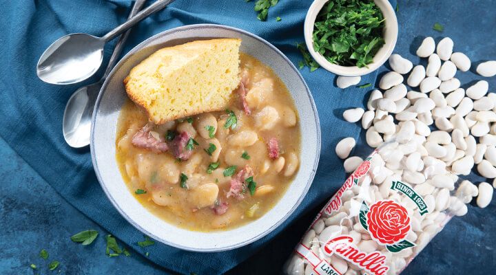 a bowl of soup with beans, bread and parsley next to it on a blue cloth