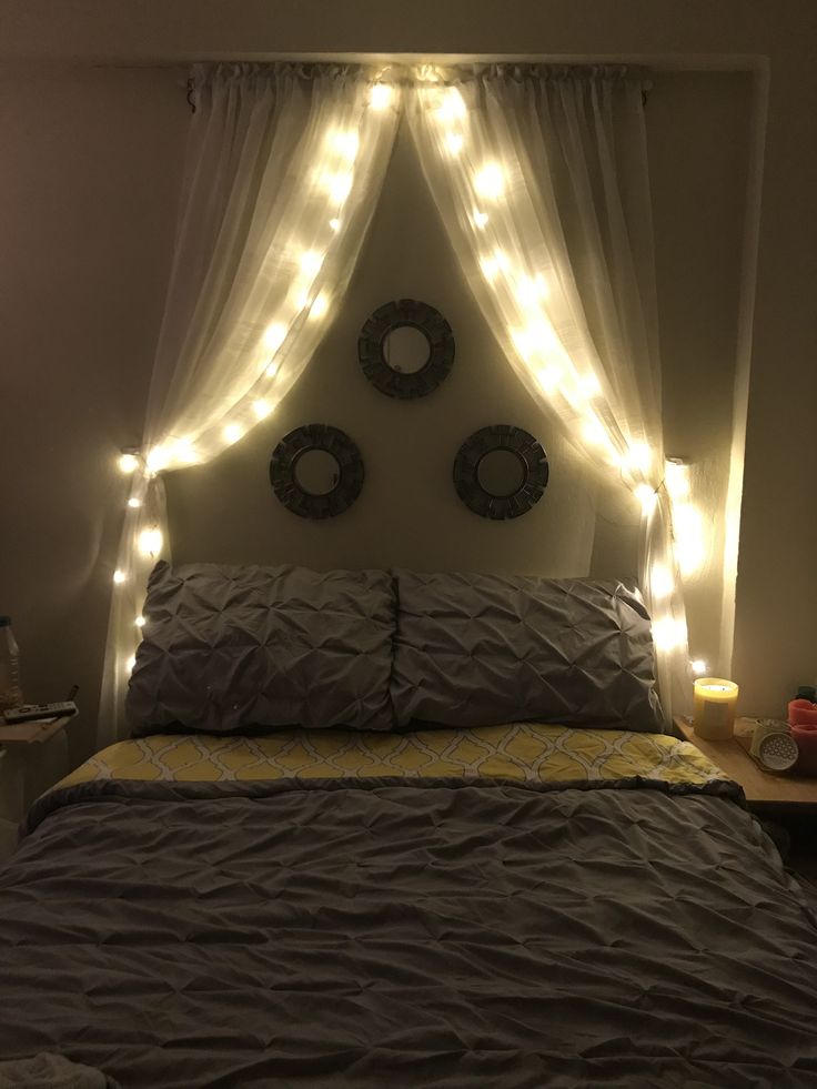 a bed that has some lights on the headboard and pillows in front of it