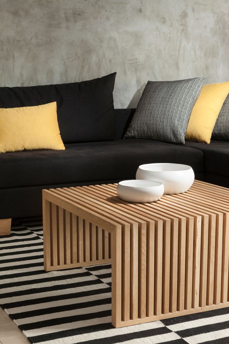 a living room with black couches and yellow pillows on the table in front of it