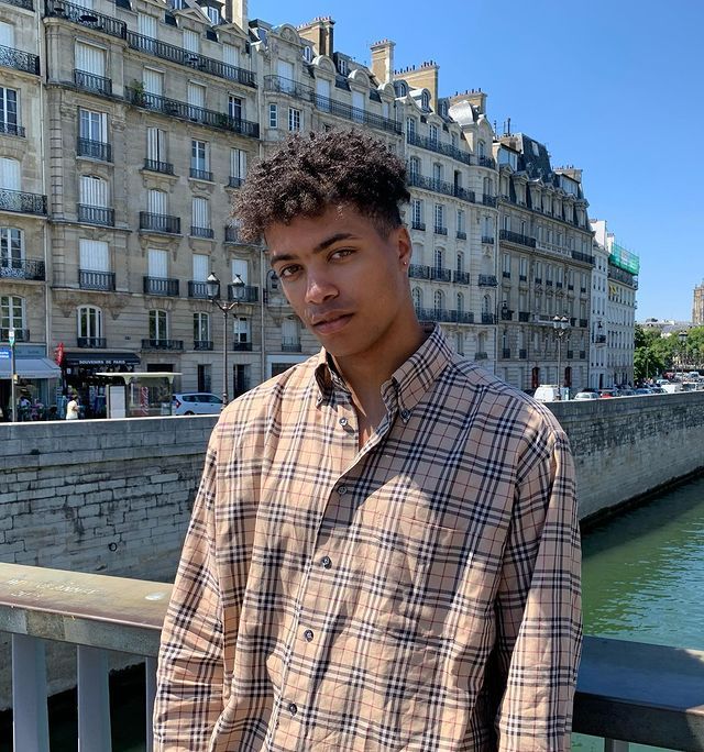 a young man standing next to a body of water in front of a cityscape