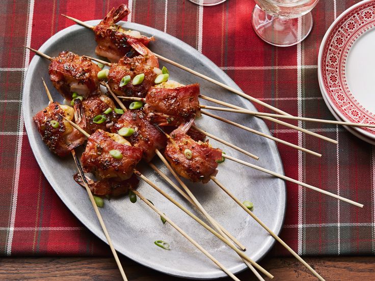 several skewered meats with sauce and green onions on a plate next to wine glasses