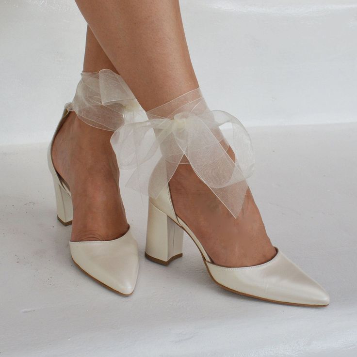 a woman's legs wearing white high heels with a sheer ribbon around the ankle