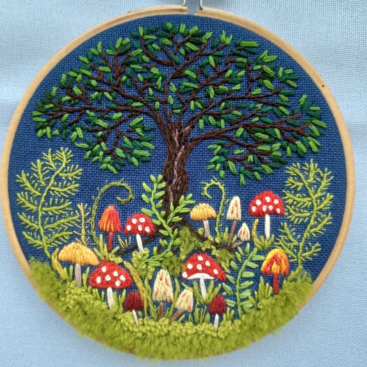 an embroidery project with mushrooms and trees in the grass, on a blue cloth background