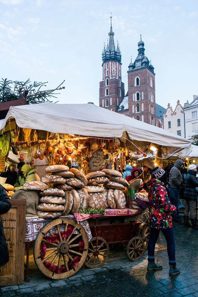 an outdoor market with lots of food and people standing around it in front of some buildings