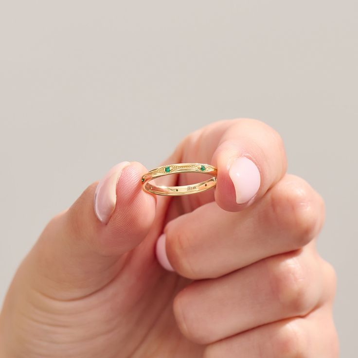 a woman's hand holding a gold ring with green stones on it and her fingers