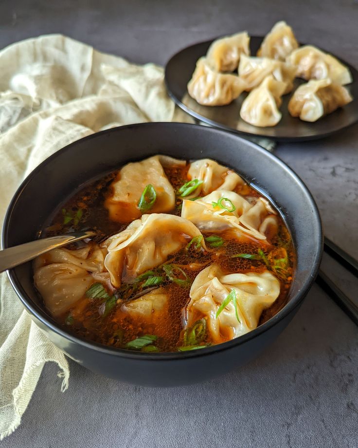 two black plates filled with dumplings next to chopsticks and a white cloth