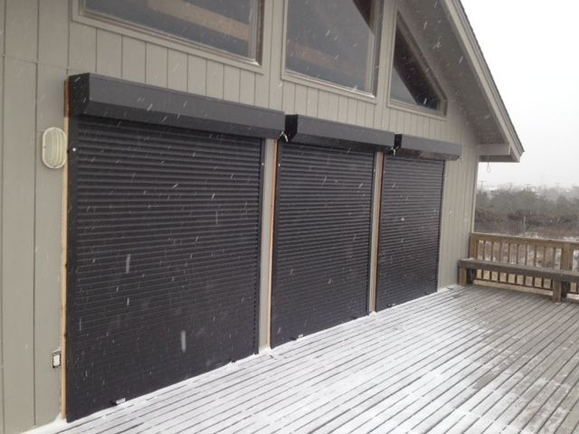 an open garage door on the side of a house with snow falling off it's roof