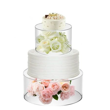 three tiered wedding cake with pink and white flowers on the bottom, in front of a white background