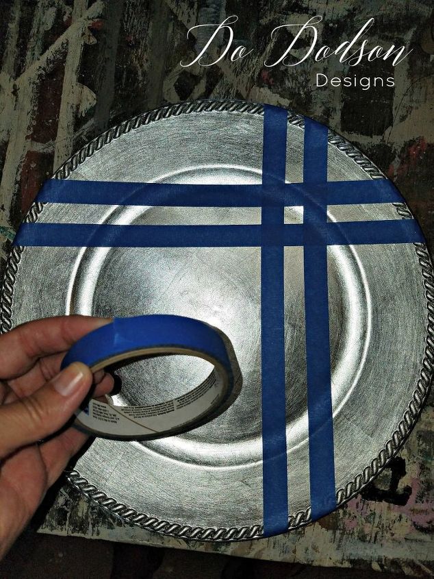 a person is holding a blue and silver plate with a cross on it, in front of a wall