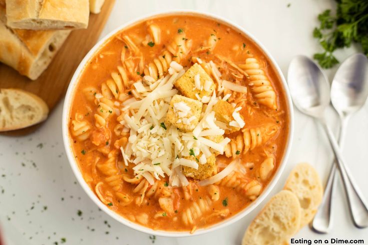 a bowl of pasta soup with bread and parmesan cheese on the side next to it