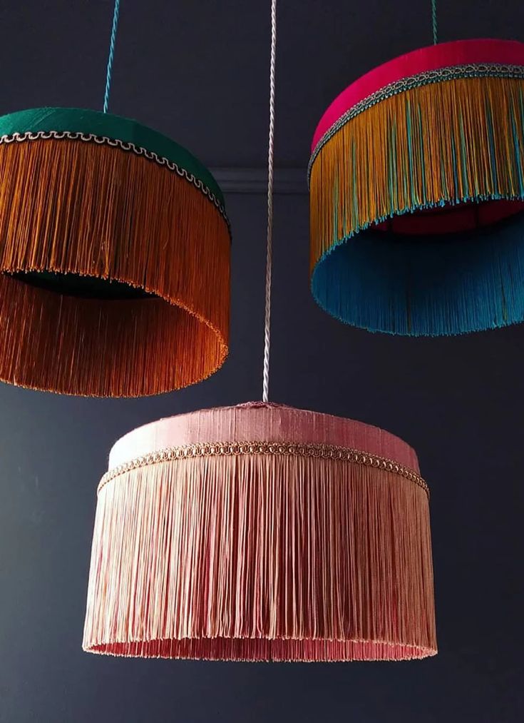 three colorful lamps hanging from the ceiling with fringes on each lamp shade and one light fixture in different colors