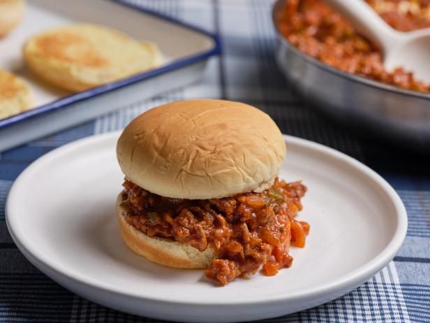 a sloppy joe sandwich sitting on top of a white plate next to some other food