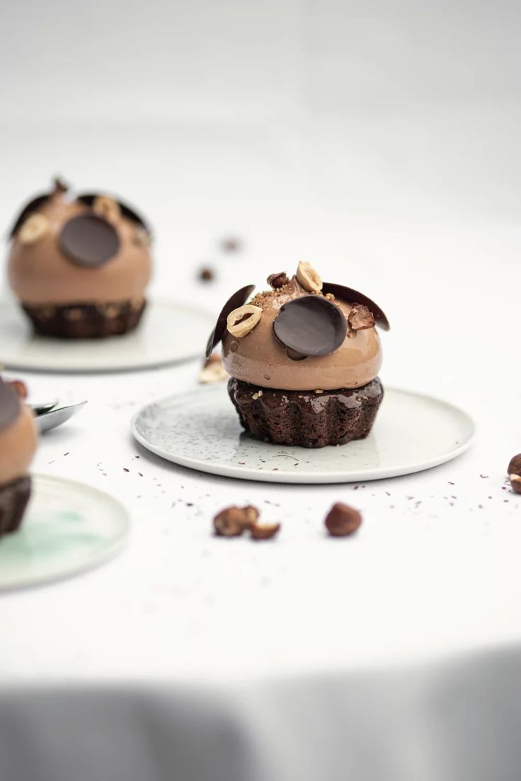 three chocolate cupcakes with frosting and nuts on the top, sitting on plates