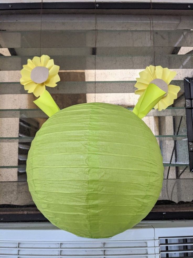 a green paper ball with two yellow flowers on it's head hanging from the ceiling