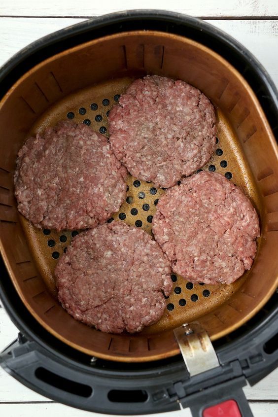 hamburger patties in an air fryer basket on top of a white wooden table